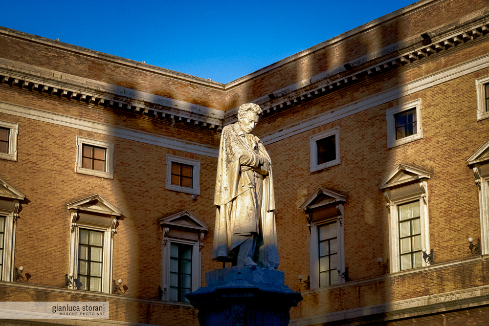 La statua di Leopardi illuminata dal sole e l'ombra della torre di Recanati