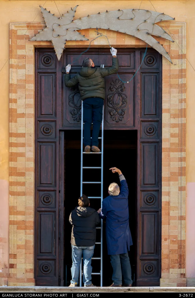 Tre uomini sistemano le luminarie della chiesa Santa Croce di Macerata
